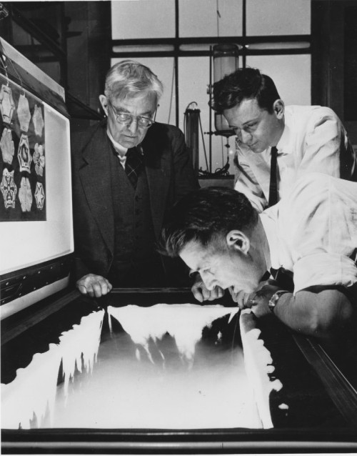 On the left physicist Bernard Vonnegut, Brother of Vincent Schaefer. Vincent Schaefer on the right, and Nobel winner Irving Langmuir standing with glasses next to Bernard Vonnegut. They are seeding a snow cloud in Schaefer’s ice box.